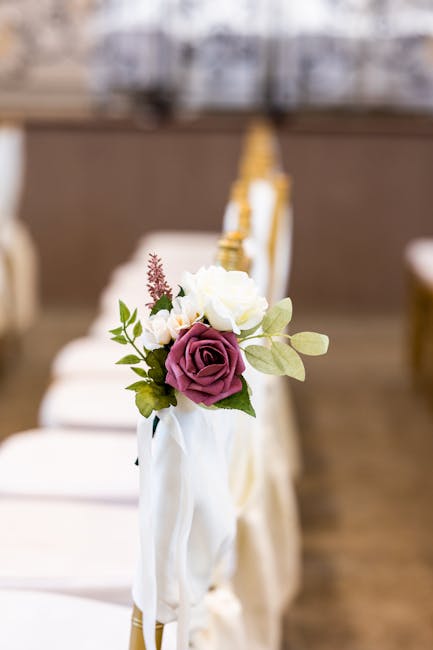 Close-up of a floral arrangement featuring a bouquet with a deep purple rose, white roses, and small pink and white accent flowers with green foliage, attached to a light-colored chair with white fabr