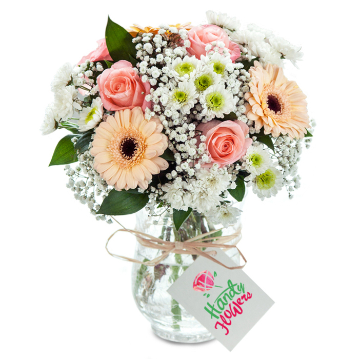 Framed against a clean, luminous background, this bouquet unites romance and cheer in the distinctive style of Tolworth floristry. Lush peach-pink roses, their velvety petals gently furled, are joined by exuberant peach gerberas whose deep brown centres radiate happiness. Fountains of white gypsophila drift among the larger flowers, creating an ethereal fullness like the wide expanses near King Charles Road. Interspersed white chrysanthemums, some with pale green hearts, evoke the freshness found in local parks and gardens. Deep green eucalyptus leaves weave a modern accent throughout, grounding the arrangement and adding subtle fragrance. The clear, subtly textured glass vase supports the display, with stems visible in cool water. Around the vase's neck, a rustic twine ribbon is tied in an informal bow, suspending a minimalist white tag suitable for a note or greeting. Crafted with the attentive eye of a Tolworth florist, this bouquet is ideal for expressing appreciation, commemorating milestones, or welcoming guests into a bright, hopeful space.