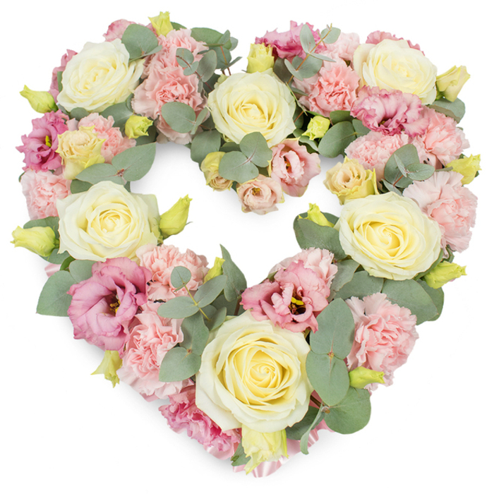 A beautifully composed heart-shaped funeral tribute fills the frame, framed by a stark white background that allows every pastel nuance to stand out. The heart is densely arranged so that no gaps remain, giving the impression of abundance and steady, unwavering affection. Large cream and pale yellow roses are spaced throughout the design, their velvety, spiralling petals opening like soft shells, each one an anchor point in the composition. Between them, clusters of soft pink carnations, with their finely frilled edges and layered petals, create a gentle, quilted effect, smoothing the contours of the heart. Interspersed among the pastels are deeper pink and mauve lisianthus flowers, some fully open, others only partially unfurled, their slightly ruffled petals and darker centres introducing quiet depth and contrast, similar to the way shadows fall in the late afternoon around Tolworth's residential streets. Winding between the blooms, sprigs of silvery-green eucalyptus bring a cool, calming element, the rounded leaves and smooth texture offsetting the frills and folds of the blossoms. Small yellow-green buds peep out at intervals, symbolising freshness and continuity even in the context of loss. The arrangement feels thoughtful and intimate, like something prepared in a neighbourhood florist on Tolworth Broadway by someone who understands the delicate nature of farewell flowers. This heart-shaped wreath would be fitting for display next to a coffin, in front of the lectern during a service, or beside a photograph at a wake, offering families in Tolworth a soft but eloquent way to honour a loved one with sympathy, respect, and enduring love.